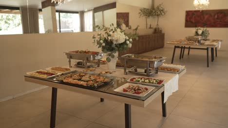 elegant buffet setup with trays of appetizers, pastries, and decorative floral arrangements on tables, ready for a gathering