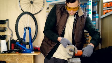 tilt-up shot of mechanic working with electric circular saw fixing small metal part. shielding spectacles and protective gloves, bicycle spare parts and tools are visible.