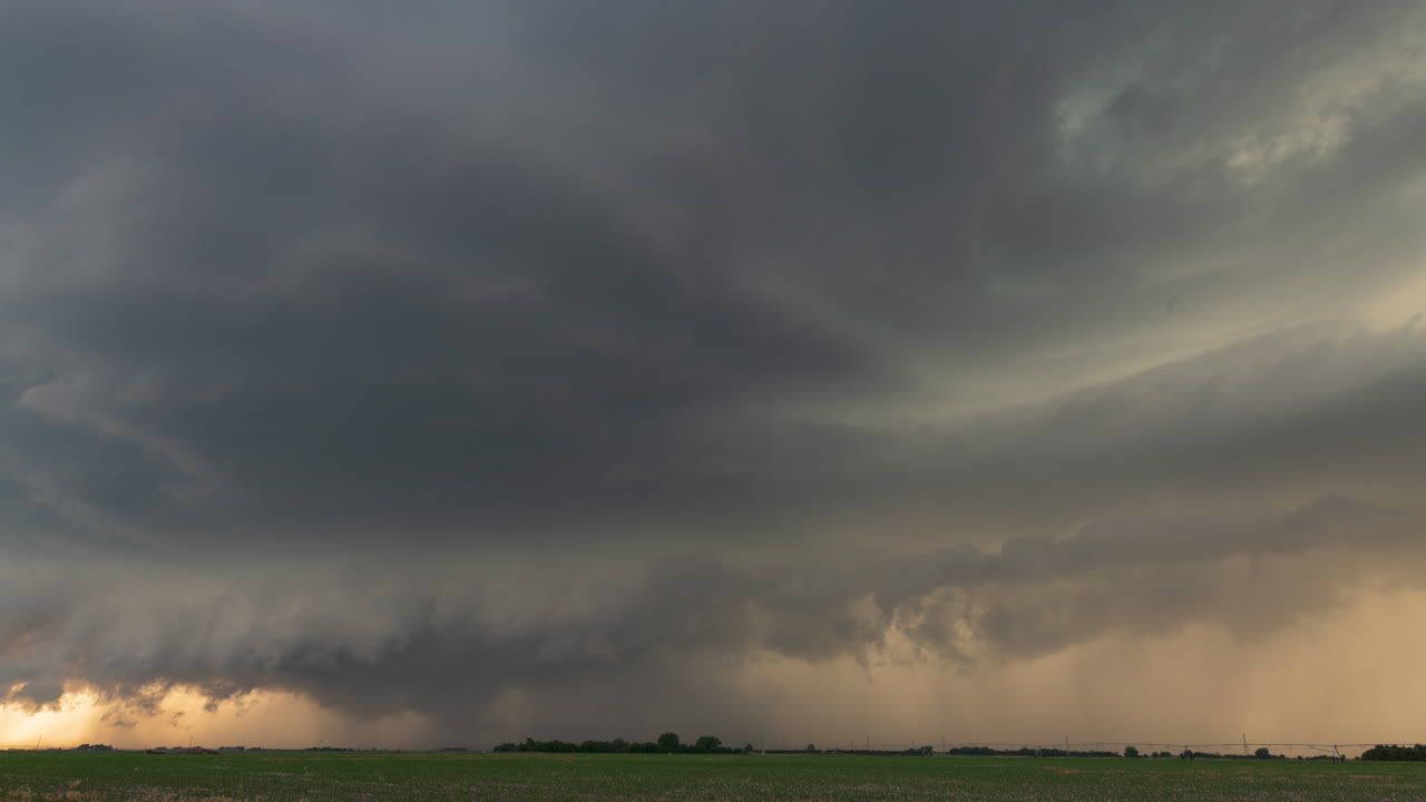 En tornado-varslet supercelle nærmer sig vores position, mens solen begynder at gå ned, hvilket skaber et orange skær på himlen.