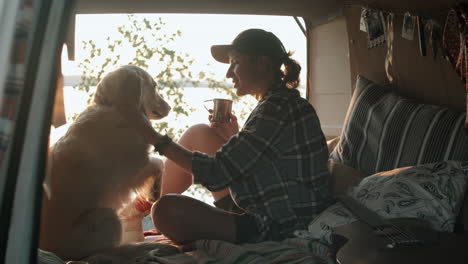 female tourist having tea while sitting with dog in van at sunset