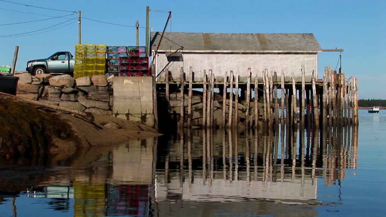 At a lobster village in Stonington Maine stacks of cages are near a truck parked outside a building over water