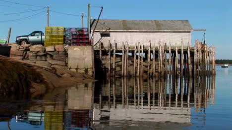 In-Einem-Hummerdorf-In-Stonington-Maine-Stehen-Stapel-Von-Käfigen-In-Der-Nähe-Eines-Lastwagens,-Der-Vor-Einem-Gebäude-über-Wasser-Geparkt-Ist