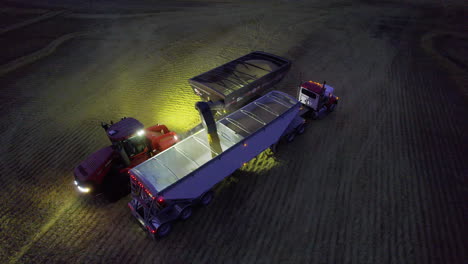 Night-aerial-view-of-grain-being-unloaded-onto-grain-hopper-trailer-behind-truck