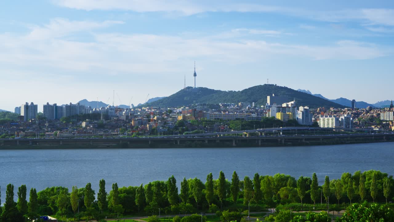 Iconic Seoul cityscape featuring Namsan Tower, the lush Hangang Park, and traffic on the Gangbyeongbuk-ro expressway - Beautiful static aerial view