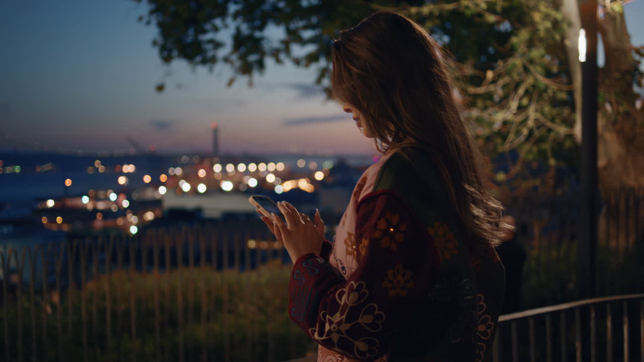 스마트폰으로 어두운 도시 관측 갑판에 서 있는 여성. 타이핑하는 여성
