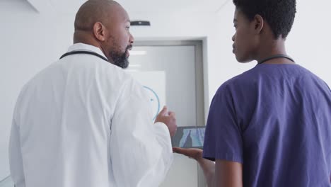 African-american-male-and-female-doctors-using-tablet,-talking-at-hospital