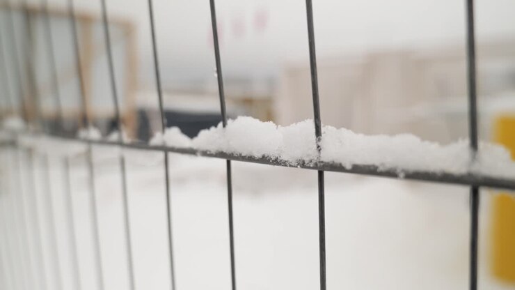 Guardando attraverso la recinzione in rete nel cantiere, dove c'è neve ovunque.