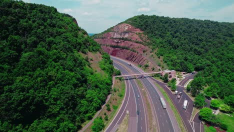 Epic-aerial-following-semi-truck-driver-with-dry-van-trailer-between-hills-in-Maryland-USA