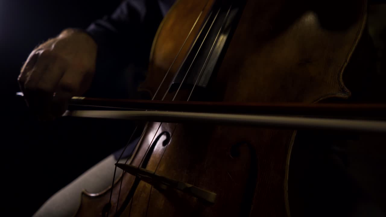 violonchelista tocando notas largas y legatos en su violonchelo con fondo negro y luz detrás