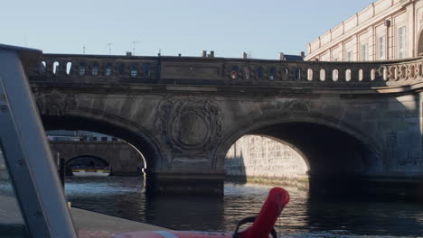 Boat-tour-approaching-ornate-stone-bridge-in-Copenhagen,-Denmark