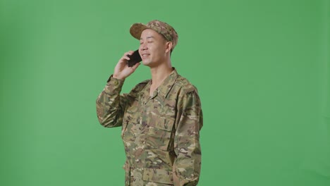 side view asian man soldier talking on smartphone and looking around while standing in the green screen background studio