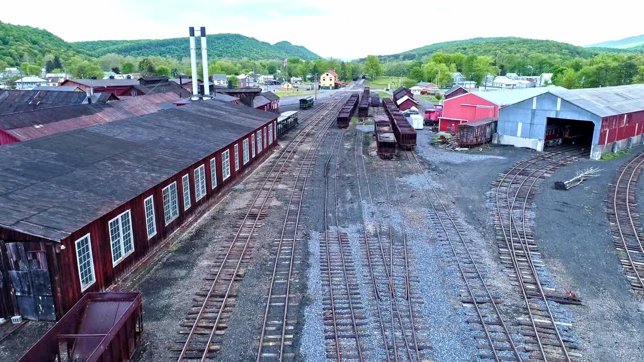 una vista aérea de una carretera ferroviaria de carbón de vía estrecha abandonada con tolvas oxidadas y vagones de carga y un edificio de apoyo que comienza a restaurarse