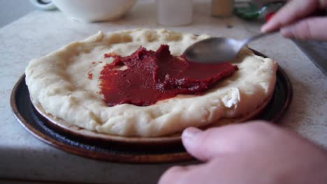 esparciendo la pasta de tomate en la base de la pizza preparada