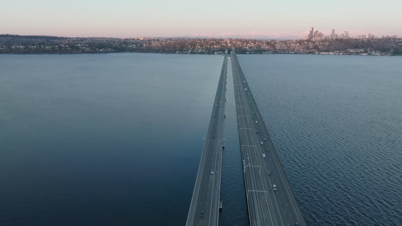 Cinematic drone flight showcases the stunning islands of Seattle, Washington. Cars cross the floating bridge connecting the islands, with the blue waters of lake and the city skyline in the background