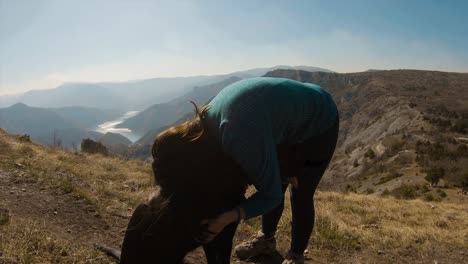 chica abrazándose con un perro labrador negro en una montaña con un hermoso cañón lacustre en el fondo
