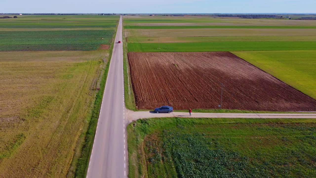녹색 초원과 농작물로 둘러싸인 직선 도로를 따라 빨간 자동차가 혼자 운전합니다.