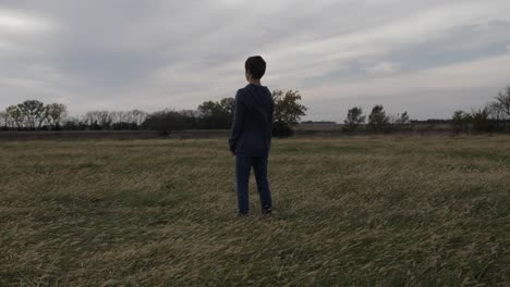 a teen boy stands in a kansas field by himself watching the sun setting