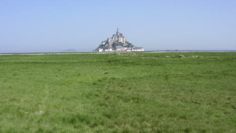 low altitude flight towards mont saint-michel across green grass fields