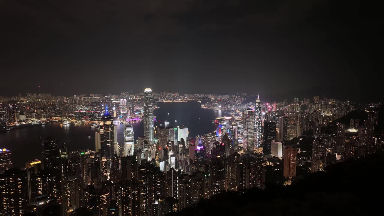 Timelapse toàn cảnh tuyệt đẹp về đêm, di chuyển sang trái trên đường chân trời dày đặc của Hồng Kông và Cảng Victoria rực rỡ ánh đèn neon từ Đỉnh Victoria