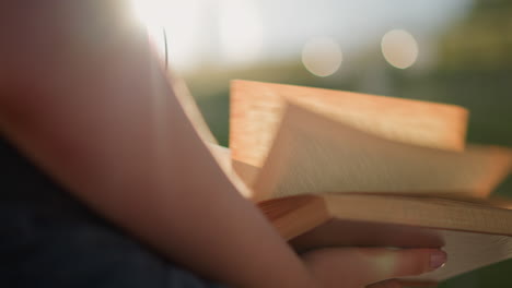 close-up of individual holding book, flipping through pages as sunlight reflects on the person, the blurred background shows two glowing light effects