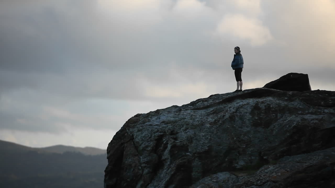 una mujer mira a lo lejos en un alto acantilado
