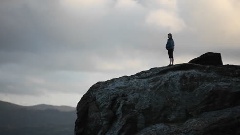 A-woman-looks-out-into-the-distance-on-a-high-cliff