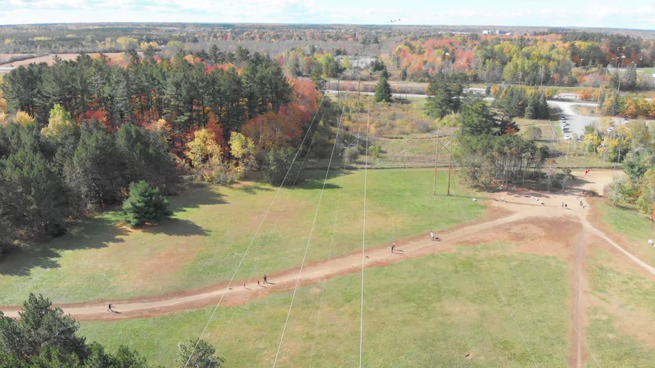 Riprese aeree lente rivolte verso il basso su un sentiero pedonale e linee elettriche a Ottawa, Ontario, con escursionisti e una foresta soleggiata dai colori autunnali in lontananza.