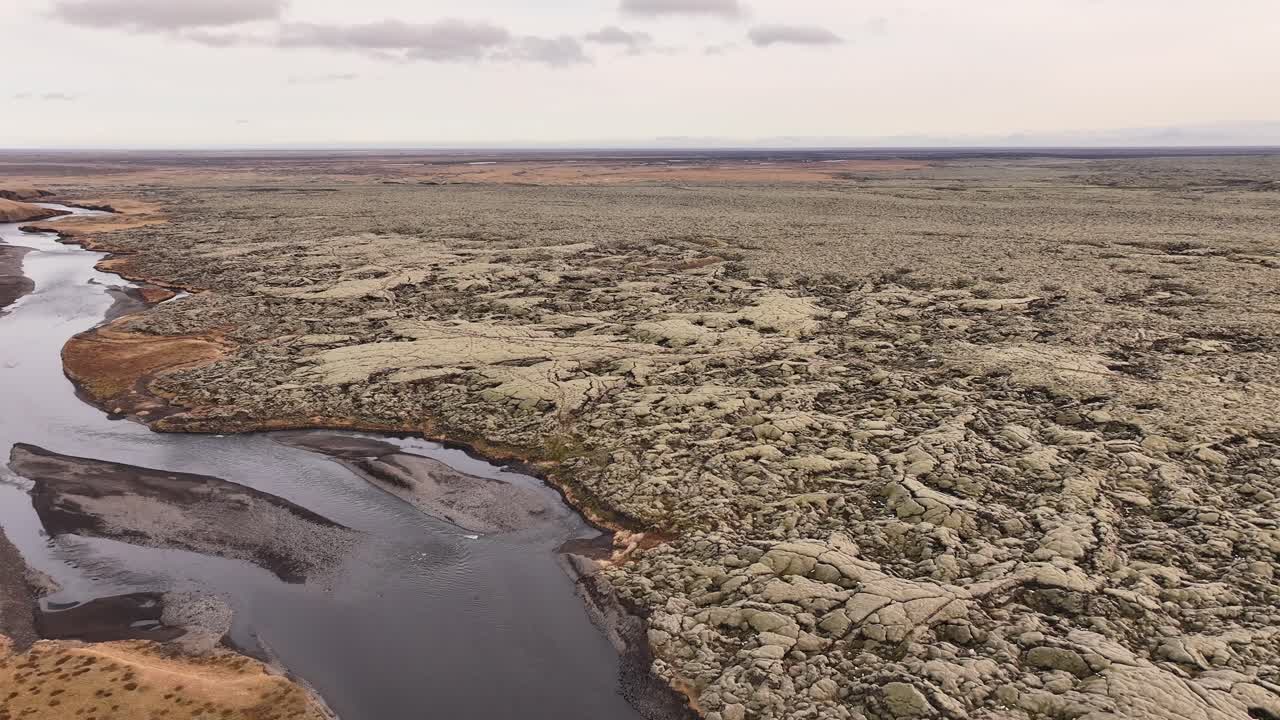 Aerial view over vast cracked lava fields and winding river near Fjaðrárgljúfur Canyon, Iceland, rugged volcanic terrain and dramatic earth textures.