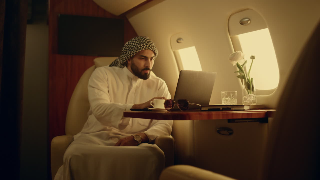 Focused man typing laptop on jet. Thinking muslim browse internet in first class