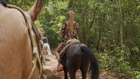 toma trasera en cámara lenta de una pareja montando a caballo en línea dentro del camino del bosque tropical desde la perspectiva del caballo en cancún, méxico