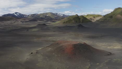 aerial approaching shot of red crater volcano and snowy mountain peak in background, iceland