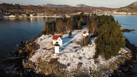 low and slow aerial fly over of snow covered curtis island lighthouse at sunrise with long shadows in the snow