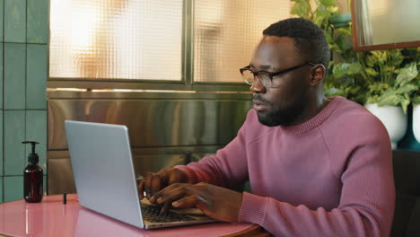 hombre afroamericano escribiendo en una computadora portátil en un café