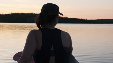 woman in a canoe points across calm water at golden hour