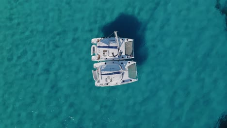 Aerial-top-down-drone-view-of-2-sailing-yachts-floating-side-by-side-as-they-anchor-in-shallow-Spanish-bay