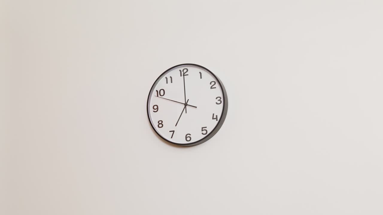 A wide 4K shot of a classic black and white wall clock on a plain white wall, displaying the time as X:00.
