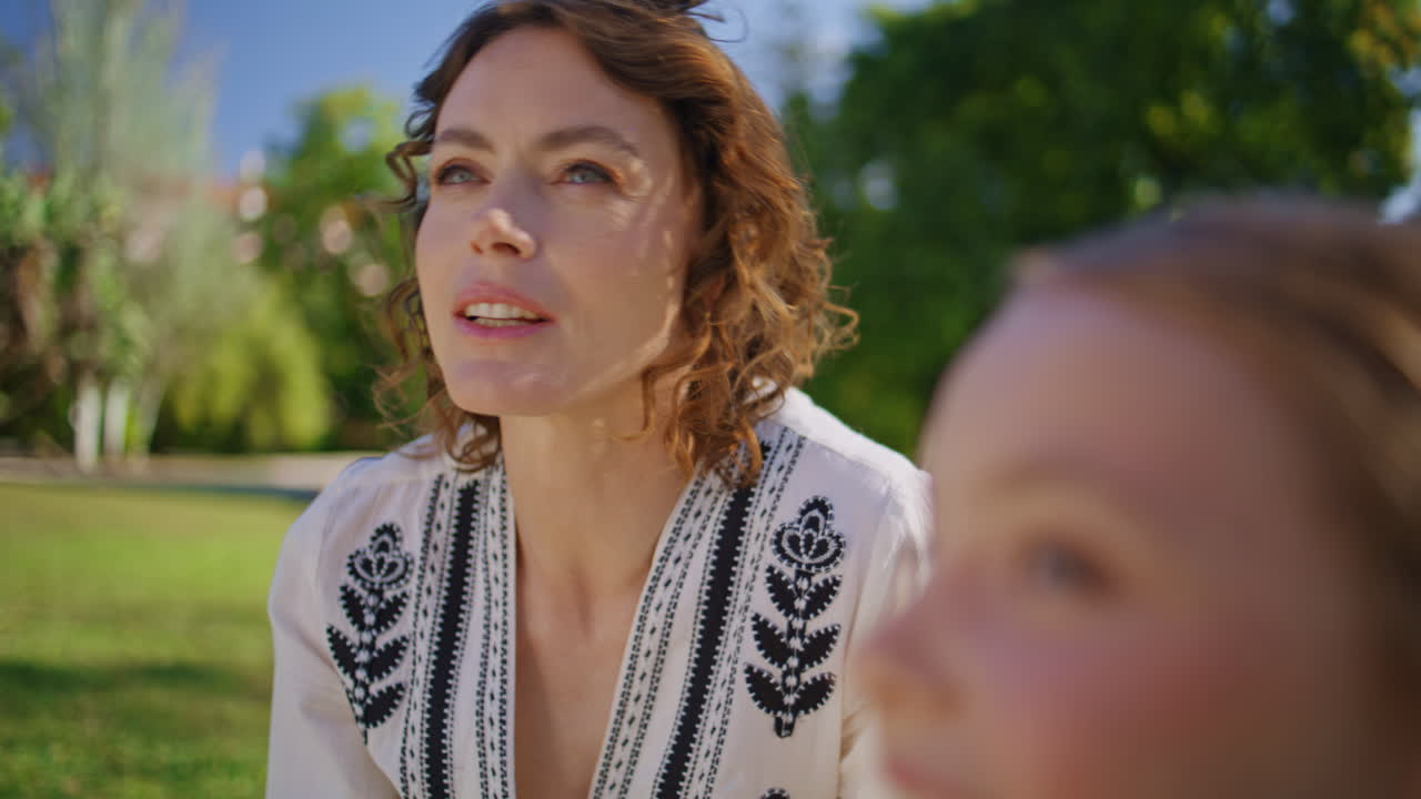 Smiling woman sitting grass listening little daughter in park picnic closeup