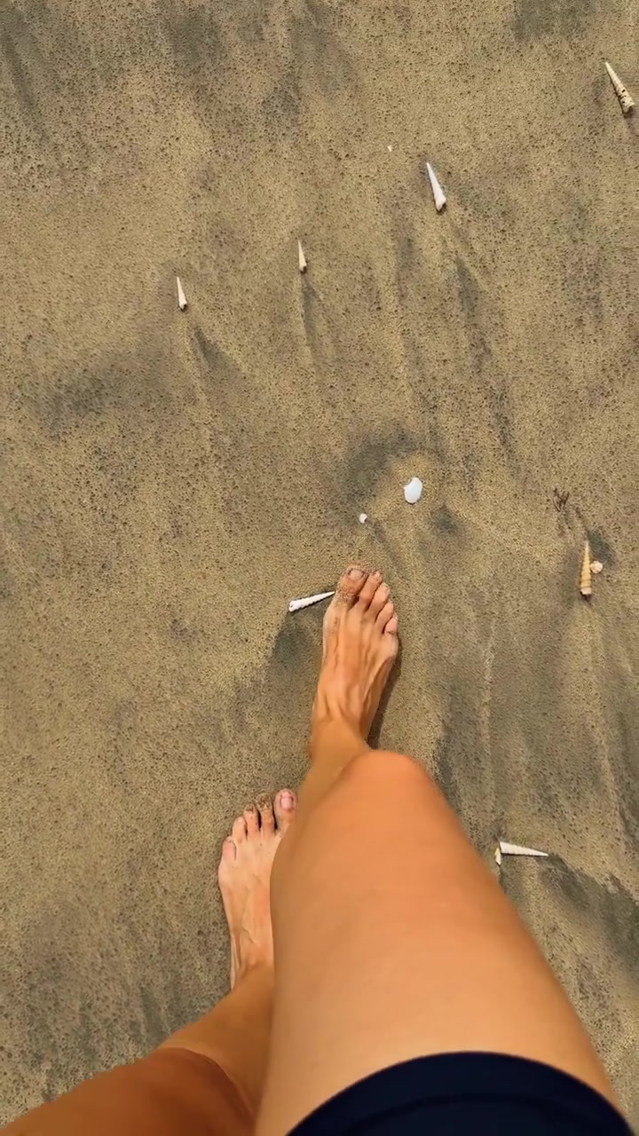 Piedi che camminano sulla sabbia bagnata tra le conchiglie, Costa Rica. Prospettiva personale dall'alto di dita sabbiose con conchiglie a spirale sparse.