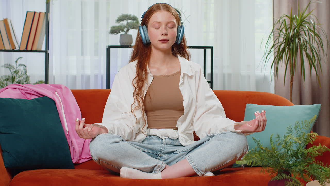 una adolescente pelirroja respira profundamente con un gesto de mudra, ojos cerrados, meditando, escuchando música