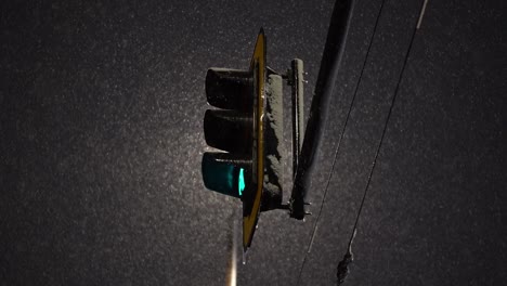 backlit streetlight changes from green to yellow as snow falls in slow motion