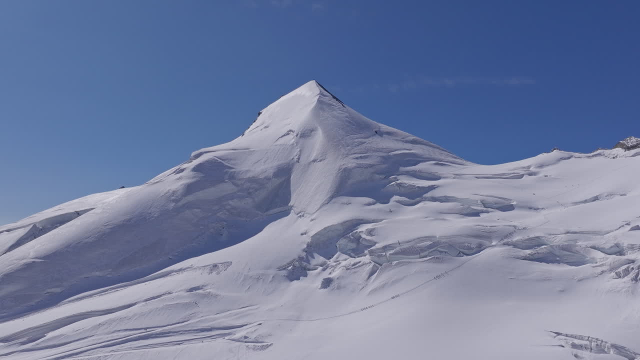 A powerful drone shot revealing massive overhanging seracs and towering ice cliffs in Saas-Fee, Switzerland. The frozen formations glisten under alpine light, showcasing the raw power of the glacier
