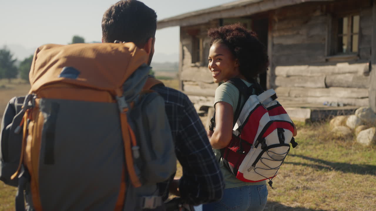 Rear View Of Group Of Friends With Backpacks Hiking In Countryside Together