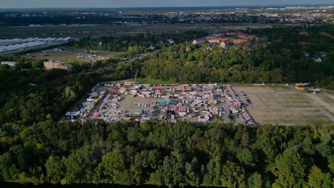 Berlin funfair showing a Ferris wheel, amusement rides, and various stalls from an aerial perspective. Dramatic aerial view flight wide orbit overview drone