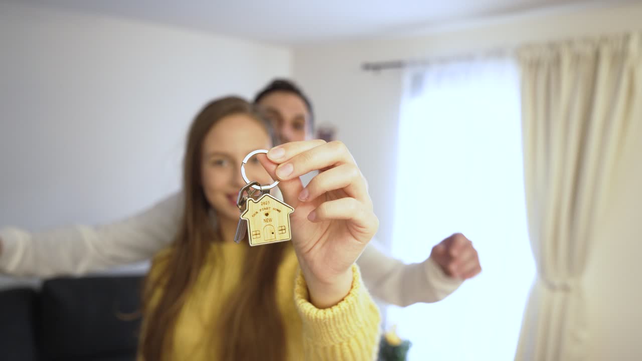 La coppia sorride raggiante mentre la donna mostra la chiave della loro nuova casa. La chiave è al centro della scena e rappresenta i sogni realizzati e l'emozione di un nuovo inizio.