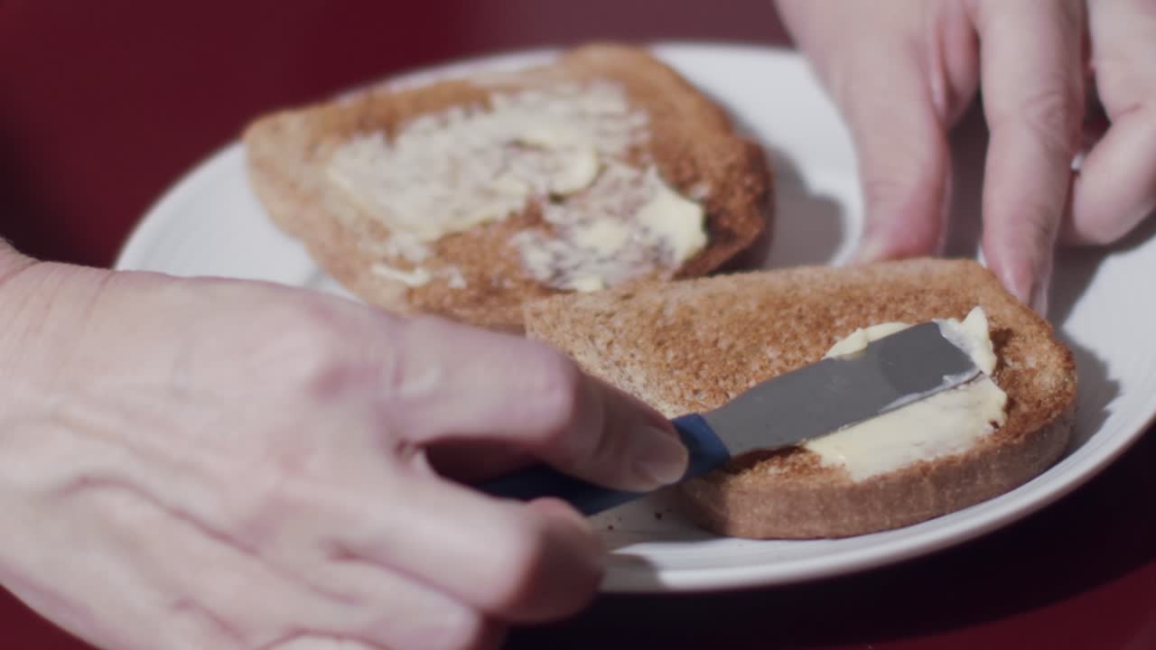caucasian hands smearing butter on toast lying on a plate in close up and slow motion
