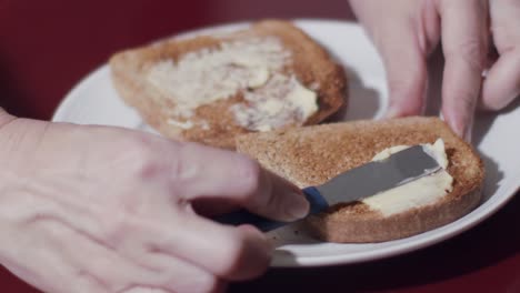 caucasian hands smearing butter on toast lying on a plate in close up and slow motion