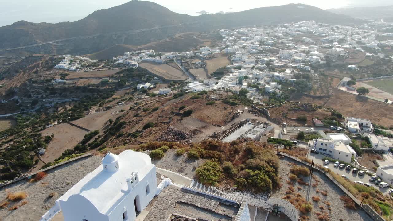 vista de avión no tripulado en grecia volando sobre una pequeña iglesia blanca en la parte superior de una colina marrón con una casa blanca griega ciudad frente al mar azul en una montaña