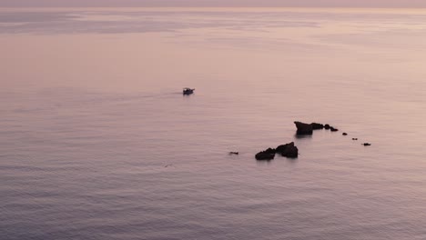 Un-Barco-Pescador-Navega-Por-Rocas-Expuestas-Hacia-El-Océano-Abierto-Mientras-El-Agua-Brilla-De-Color-Naranja