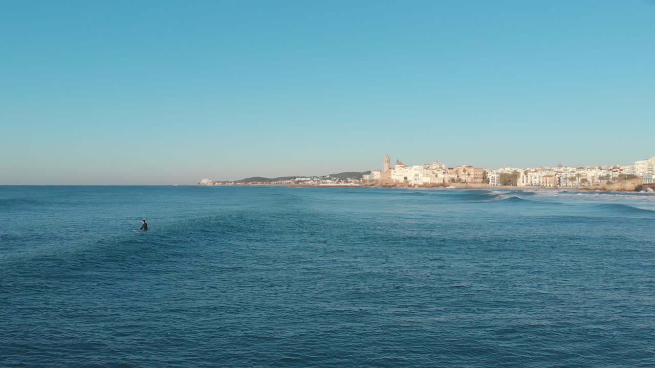 el disparo de un dron vuela sobre el mar en calma mientras el surfista espera las olas durante las horas de la mañana