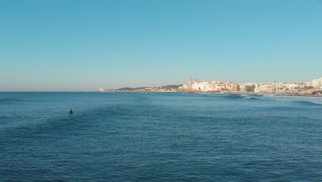 El-Disparo-De-Un-Dron-Vuela-Sobre-El-Mar-En-Calma-Mientras-El-Surfista-Espera-Las-Olas-Durante-Las-Horas-De-La-Mañana